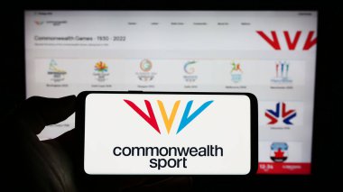 Stuttgart, Almanya - 07-30-2023: İnternet sayfası önünde ekranda Commonwealth Games Federation (CGF) organizasyonu logosu bulunan cep telefonu sahibi kişi. Telefon ekranına odaklan.