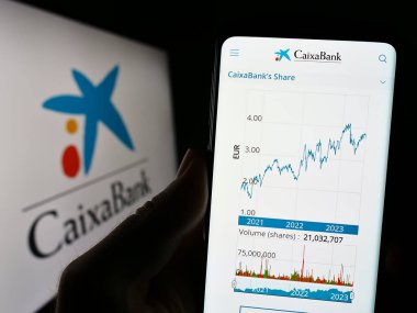 Stuttgart, Almanya - 07-30-2023: İspanyol finans şirketi CaixaBank S.A. 'nın internet sitesi ile cep telefonu tutan kişi logonun önünde ekranda. Telefon ekranının merkezine odaklan.