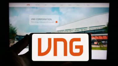 Stuttgart, Germany - 07-31-2023: Person holding smartphone with logo of Vietnamese technology company VNG Corporation on screen in front of website. Focus on phone display. clipart