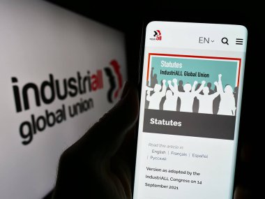 Stuttgart, Almanya - 07-31-2023: Endüstriyel Küresel Birlik web sitesi ile logo önünde cep telefonu tutan kişi. Telefon ekranının merkezine odaklan.