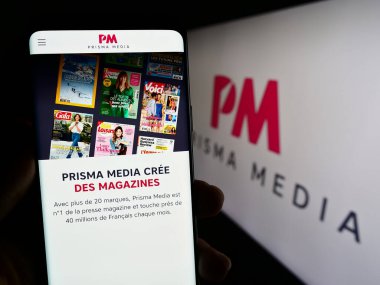 Stuttgart, Germany - 08-01-2023: Person holding cellphone with web page of French publishing company Prisma Media on screen in front of logo. Focus on center of phone display. clipart