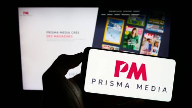 Stuttgart, Germany - 08-01-2023: Person holding cellphone with logo of French publishing company Prisma Media on screen in front of business webpage. Focus on phone display. clipart