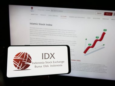 Stuttgart, Germany - 08-02-2023: Person holding smartphone with logo of financial market Indonesia Stock Exchange (IDX) on screen in front of website. Focus on phone display. clipart