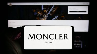Stuttgart, Almanya - 08-02-2023: İtalyan moda şirketi Moncler SpA 'nın logosuyla cep telefonu tutan kişi iş sayfasının önünde ekranda. Telefon ekranına odaklan.