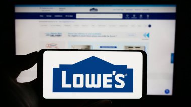 Stuttgart, Almanya - 08-02-2023: ABD 'li perakende şirketi Lowe' s Companies Inc. 'in logosuyla cep telefonu sahibi kişi iş sayfasının önünde ekranda. Telefon ekranına odaklan.