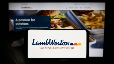 Stuttgart, Almanya - 08-02-2023: Web sitesi önünde ekranda ABD 'li patates şirketi Lamb Weston Holding Inc.' in logosunun bulunduğu akıllı telefon sahibi kişi. Telefon ekranına odaklan.