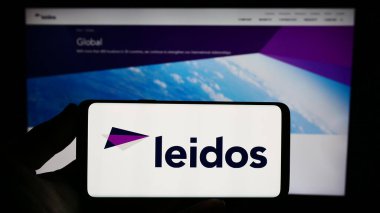 Stuttgart, Almanya - 08-02-2023: ABD 'li savunma şirketi Leidos Inc.' in logosunu elinde tutan kişi web sitesinin önünde ekranda. Telefon ekranına odaklan.