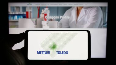 Stuttgart, Almanya - 08-04-2023: Web sitesinin önünde Mettler-Toledo International Inc. şirketinin logosuna sahip akıllı telefonu elinde tutan kişi. Telefon ekranına odaklan.