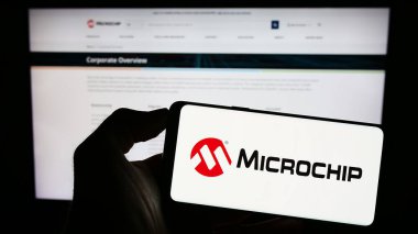 Stuttgart, Almanya - 08-04-2023: İnternet sitesi önünde ekranda üzerinde ABD 'li yarı iletken şirket Microchip Technology Inc.' in logosu bulunan akıllı telefon sahibi kişi. Telefon ekranına odaklan.
