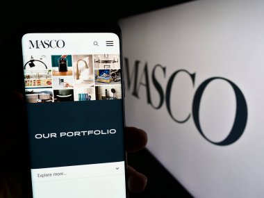 Stuttgart, Almanya - 08-04-2023: ABD 'li ev iyileştirme şirketi Masco Corporation' ın web sayfası ile cep telefonu tutan kişi logolu ekranda. Telefon ekranının merkezine odaklan.