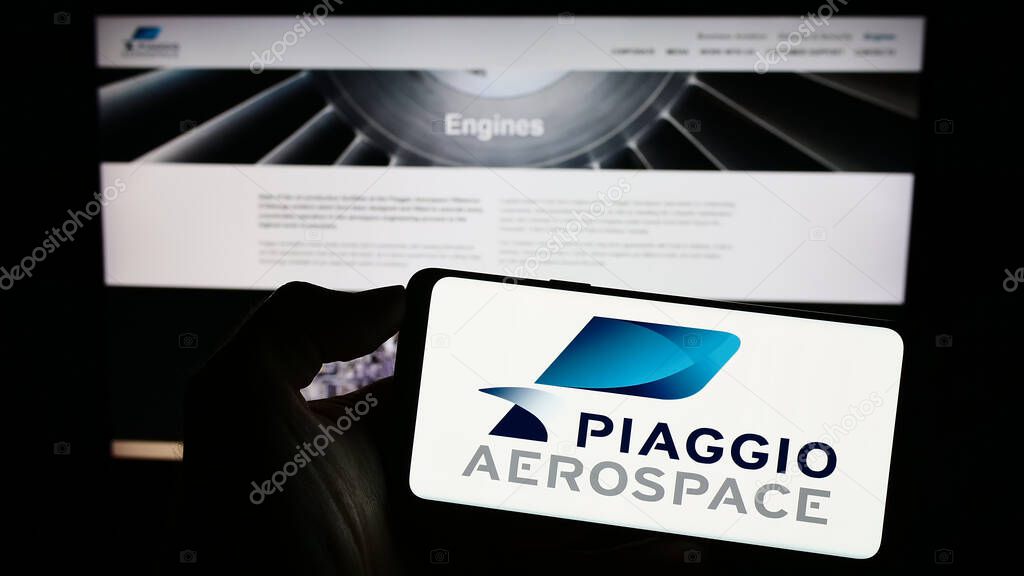 Stuttgart, Germany - 07-30-2023: Person holding cellphone with logo of Italian company Piaggio Aero Industries SpA on screen in front of business webpage. Focus on phone display.
