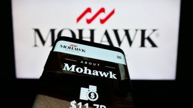 Stuttgart, Germany - 08-05-2023: Mobile phone with website of US flooring company Mohawk Industries Inc. on screen in front of business logo. Focus on top-left of phone display. clipart