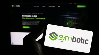 Stuttgart, Germany - 08-05-2023: Person holding smartphone with logo of US robotics warehouse company Symbotic Inc. on screen in front of website. Focus on phone display. clipart