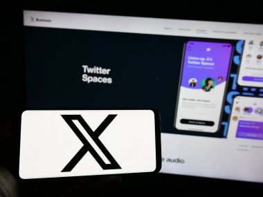 Stuttgart, Almanya - 08-05-2023: İnternet sayfası önünde üzerinde Amerikan sosyal medya şirketi X Corp. (Twitter) logosu bulunan cep telefonu sahibi kişi. Telefon ekranına odaklan.