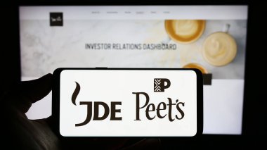 Stuttgart, Almanya - 08-05-2023: İçki şirketi JDE Peet 'in NV' sinin logosuyla cep telefonu sahibi kişi iş sayfasının önünde ekranda. Telefon ekranına odaklan.