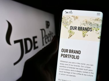 Stuttgart, Almanya - 08-05-2023: İçecek şirketi JDE Peet 'in N.V.' nin web sitesi olan cep telefonu sahibi iş logosu önünde ekranda görülüyor. Telefon ekranının merkezine odaklan.