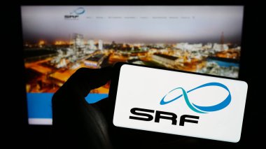 Stuttgart, Germany - 08-05-2023: Person holding cellphone with logo of Indian chemicals company SRF Limited on screen in front of business webpage. Focus on phone display. clipart