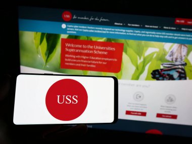 Stuttgart, Almanya - 08-05-2023: İnternet sitesi önünde ekranda Üniversiteler Denetim Şeması (USS) logosu bulunan akıllı telefon sahibi kişi. Telefon ekranına odaklan.