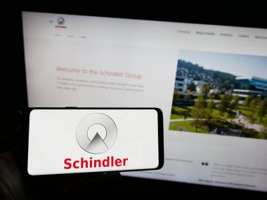 Stuttgart, Almanya - 08-05-2023: İsviçreli asansör şirketi Schindler Group 'un logosuyla cep telefonu sahibi kişi iş sayfasının önünde ekranda. Telefon ekranına odaklan.