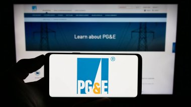 Stuttgart, Almanya - 08-05-2023: İnternet sayfası önünde ekranda ABD 'li kamu kuruluşu Pacific Gas ve Electric Company' nin (PGE) logosuna sahip cep telefonu bulunan kişi. Telefon ekranına odaklan.