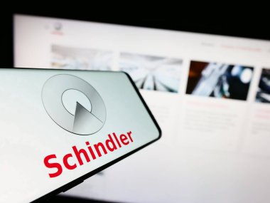 Stuttgart, Almanya - 08-05-2023: İsviçreli asansör şirketi Schindler Group 'un logosunun yer aldığı cep telefonu iş sitesinin önünde ekranda. Telefon ekranının merkezine odaklan.