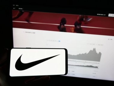 Stuttgart, Almanya - 08-06-2023: Üzerinde Amerikan spor giyim şirketi Nike Inc. 'in logosu olan cep telefonu sahibi kişi iş sayfasının önünde ekranda. Telefon ekranına odaklan.