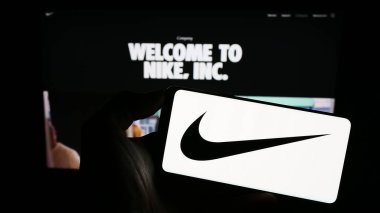 Stuttgart, Almanya - 08-06-2023: ABD 'li spor giyim şirketi Nike Inc.' in logosunu elinde tutan kişi web sitesinin önünde ekranda. Telefon ekranına odaklan.