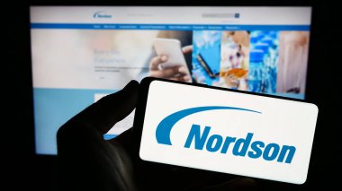 Stuttgart, Almanya - 08-06-2023: ABD 'li dağıtım şirketi Nordson Corporation' ın logosunu elinde tutan kişi web sitesinin önünde ekranda. Telefon ekranına odaklan.