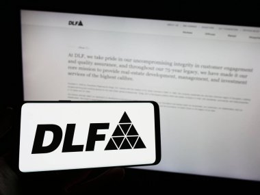 Stuttgart, Almanya - 08-06-2023: Hintli emlak şirketi DLF Limited 'in logosuna sahip cep telefonu sahibi kişi iş sayfasının önünde ekranda görülüyor. Telefon ekranına odaklan.