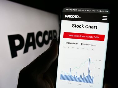 Stuttgart, Almanya - 08-06-2023: ABD 'li ticari araç şirketi PACCAR Inc.' nin web sitesi ile cep telefonu elinde tutan kişi logonun önünde ekranda. Telefon ekranının merkezine odaklan.
