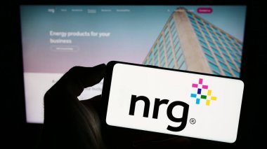 Stuttgart, Germany - 08-06-2023: Person holding smartphone with logo of US utility company NRG Energy Inc. on screen in front of website. Focus on phone display. clipart