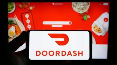 Stuttgart, Almanya - 07-25-2023: ABD 'li gıda dağıtım şirketi DoorDash Inc.' in logosunu elinde tutan kişi web sitesinin önünde ekranda. Telefon ekranına odaklan.