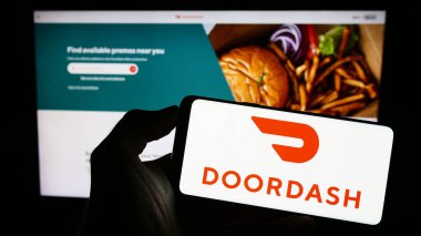 Stuttgart, Almanya - 07-25-2023: ABD 'li gıda dağıtım şirketi DoorDash Inc.' in logosuyla cep telefonu sahibi kişi iş sayfasının önünde ekranda. Telefon ekranına odaklan.