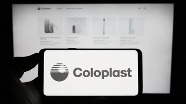 Stuttgart, Germany - 07-24-2023: Person holding mobile phone with logo of Danish healthcare company Coloplast AS on screen in front of business web page. Focus on phone display. clipart