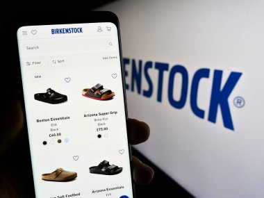 Stuttgart, Almanya - 07-24-2023: Ayakkabı şirketi Birkenstock Group B.V. Co. KG 'nin internet sayfası ile cep telefonu tutan kişi logo önünde ekranda. Telefon ekranının merkezine odaklan.