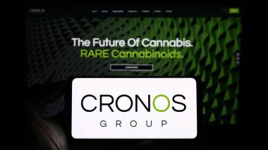 Stuttgart, Germany - 07-24-2023: Person holding smartphone with logo of Canadian cannabis company Cronos Group Inc. on screen in front of website. Focus on phone display. clipart