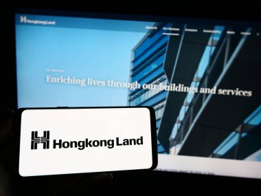 Stuttgart, Almanya - 07-22-2023: Emlak şirketi Hongkong Land Holding Limited 'in logosunun bulunduğu akıllı telefon sahibi kişi web sitesinin önünde ekranda görülüyor. Telefon ekranına odaklan.