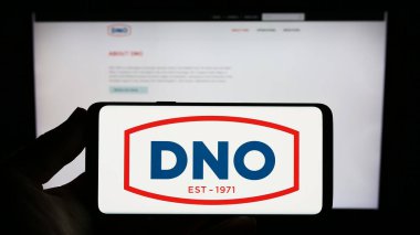 Stuttgart, Almanya - 07-21-2023: İnternet sitesi önünde Norveçli petrol ve gaz şirketi DNO ASA 'nın logosuna sahip akıllı telefonu elinde tutan kişi. Telefon ekranına odaklan.
