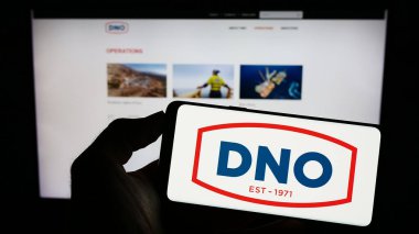 Stuttgart, Germany - 07-21-2023: Person holding cellphone with logo of Norwegian oil and gas company DNO ASA on screen in front of business webpage. Focus on phone display. clipart