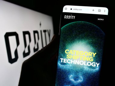 Stuttgart, Almanya - 07-21-2023: ABD 'li tüketici teknolojisi şirketi Oddity Inc.' in web sitesi ile cep telefonu elinde tutan kişi logonun önünde ekranda. Telefon ekranının merkezine odaklan.
