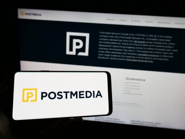 Stuttgart, Germany - 07-21-2023: Person holding mobile phone with logo of media company Postmedia Network Canada Corp. on screen in front of web page. Focus on phone display. clipart