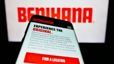 Stuttgart, Germany - 07-19-2023: Mobile phone with website of US restaurant company Benihana Inc. on screen in front of business logo. Focus on top-left of phone display. clipart