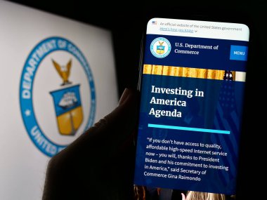 Stuttgart, Almanya - 07-15-2023: ABD Ticaret Bakanlığı 'nın (DOC) internet sayfası ile cep telefonunu mühürlü olarak ekranda tutan kişi. Telefon ekranının merkezine odaklan.