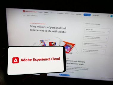 Stuttgart, Almanya - 07-15-2023: İnternet sayfası önünde üzerinde Adobe Experience Cloud (AEC) yazılım ürünü logosu bulunan cep telefonu sahibi kişi. Telefon ekranına odaklan.