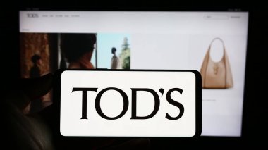 Stuttgart, Almanya - 07-15-2023: İtalyan ayakkabı şirketi Tod 'un S.P.A' sının logosuyla cep telefonu tutan kişi iş sayfasının önünde ekranda. Telefon ekranına odaklan.