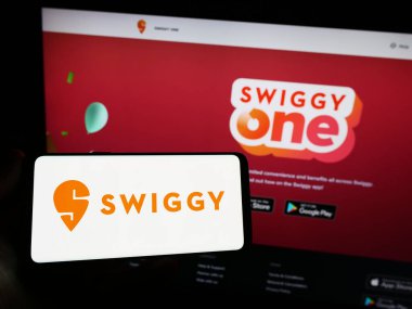 Stuttgart, Almanya - 07-15-2023: Hint gıda dağıtım şirketi Swiggy 'nin logosunu elinde tutan kişi web sitesinin önünde ekranda. Telefon ekranına odaklan.