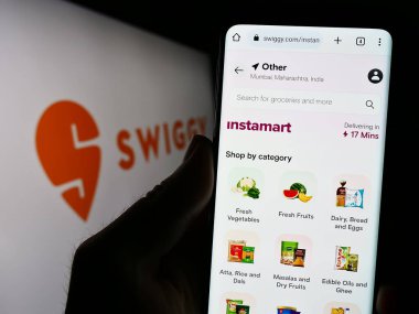Stuttgart, Almanya - 07-15-2023: Hint gıda dağıtım şirketi Swiggy 'nin web sitesi ile birlikte logo önünde cep telefonu tutan kişi. Telefon ekranının merkezine odaklan.