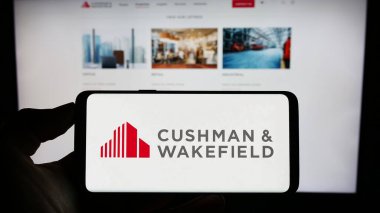 Stuttgart, Almanya - 07-15-2023: Emlak şirketi Cushman Wakefield plc 'in logosuyla cep telefonu sahibi kişi iş sayfasının önünde ekranda. Telefon ekranına odaklan.