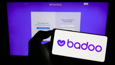 Stuttgart, Almanya - 07-15-2023: İş sayfası önünde üzerinde flört platformu Badoo (Bumble Inc.) logosu bulunan cep telefonu sahibi kişi. Telefon ekranına odaklan.