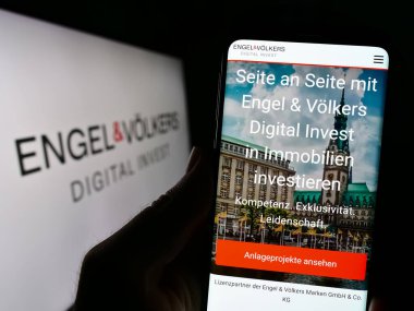 Stuttgart, Almanya - 07-15-2023: Alman emlak şirketi EV Digital Invest AG 'nin internet sayfası ile cep telefonu tutan kişi logolu ekranda. Telefon ekranının merkezine odaklan.
